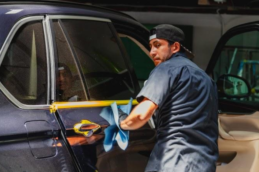 Auto body repairs. Mechanic worker burnish and polishing automobile car body by buffing grinding machine in garage workshop. Toned